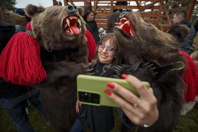 A woman takes a selfie picture with members of the Sipoteni bear pack after watching their performance in Racova, northern Romania, Tuesday, December 26, 2023. Centuries ago, people in what is now northeastern Romania would don bear fur and dance to fend off evil spirits. Nowadays, the unique custom thrives, with popular festivals drawing large crowds of locals and tourists. (Photo by Andreea AlexandruAP Photo)