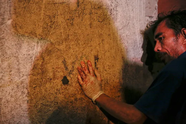 A funeral parlour worker, whose hands are bloodied from carrying bodies of killed people, rests against the wall of a house in Manila, Philippines early November 1, 2016. According to police and witnesses, unknown masked gunmen killed five people inside a house that is a known drug den. (Photo by Damir Sagolj/Reuters)