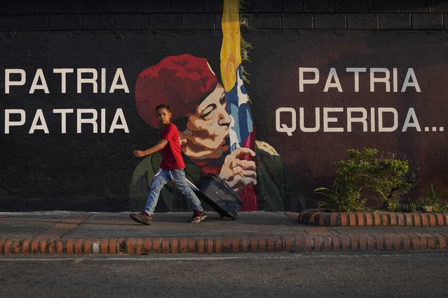 A boy pulls a suitcase on wheels as he walks past a mural of the late Venezuelan President Hugo Chavez in Chavez's hometown of Sabaneta, in Barinas state in Venezuela, Friday, January 7, 2022. The country's highest court disqualified opposition candidate Freddy Superlano as he was leading the count in November's gubernatorial election in Barinas, apparently defeating Argenis Chavez, the brother of late President Hugo Chavez's, and ordered a re-run on Jan. 9. (Photo by Matias Delacroix/AP Photo)