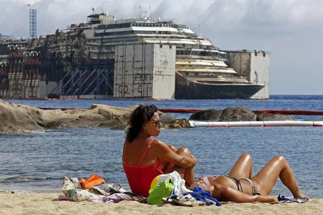 People sunbathe as the Costa Concordia cruise liner is seen during its refloating operation at Giglio harbour July 21, 2014. The massive hulk of the Costa Concordia is nearly ready to be towed away from the Italian island where it struck a rock and capsized two-and-a-half years ago, killing 32 people, officials said on Sunday. Italy on Thursday, Jan. 13, 2022, is marking the 10th anniversary of the Concordia disaster with a daylong commemoration, honoring the 32 people who died but also the extraordinary response by the residents of Giglio who took in the 4,200 passengers and crew from the ship on that rainy Friday night and then lived with the Concordia carcass for another two years before it was hauled away for scrap. (Photo by Giampiero Sposito/Reuters)