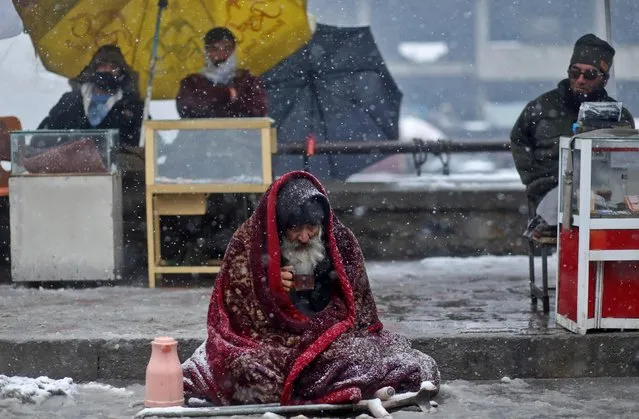 An elderly man drinks tea as he sits alongside a road during a snowfall in Kabul, Afghanistan, January 3, 2022. (Photo by Ali Khara/Reuters)
