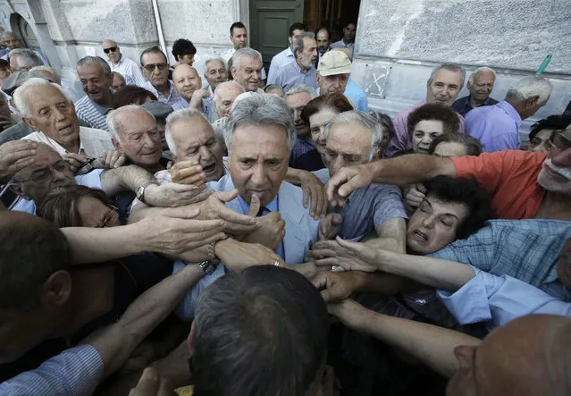 An employee of the National Bank of Greece (C) distributes priority tickets to pensioners outside a bank branch in central Athens, Greece, 01 July 2015. Pensioners who do not own an ATM card line up to enter in a bank branch to withdraw part of their pension, limit up 120 euros, as a result of capital controls imposed by the Greek government. (Photo by Yannis Kolesidis/EPA)