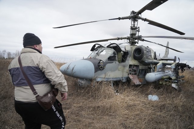 A man stands in front of a Russian Ka-52 helicopter gunship is seen in the field after a forced landing outside Kyiv, Ukraine, Thursday, February 24, 2022. Russia on Thursday unleashed a barrage of air and missile strikes on Ukrainian facilities across the country. (Photo by Efrem Lukatsky/AP Photo)