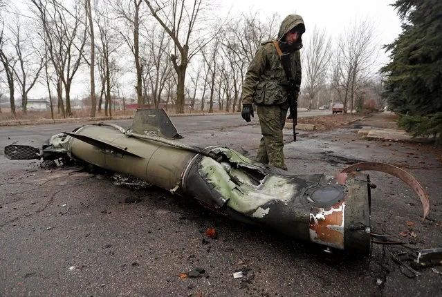A militant of the self-proclaimed Donetsk People's Republic inspects the remains of a missile that landed on a street in the separatist-controlled city of Donetsk, Ukraine on February 26, 2022. (Photo by Alexander Ermochenko/Reuters)