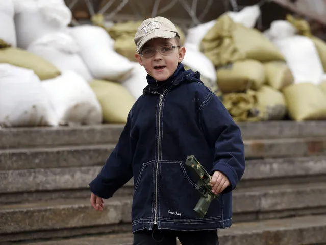A boy with a toy gun walks in front of seized regional government headquarters in Luhansk, eastern Ukraine, May 2, 2014. Ukrainian forces attacked the rebel-held city of Slaviansk before dawn on Friday and pro-Russia separatists shot down at least one attack helicopter, killing a pilot, in a sharp escalation of the conflict. (Photo by Vasily Fedosenko/Reuters)