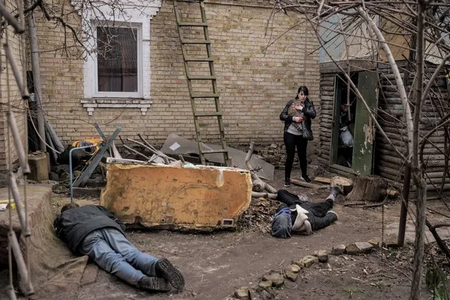 Ira Gavriluk holds her cat as she walks next to the bodies of her husband, brother, and another man, who were killed outside her home in Bucha, on the outskirts of Kyiv, Ukraine, Monday, April 4, 2022. Russia is facing a fresh wave of condemnation after evidence emerged of what appeared to be deliberate killings of civilians in Ukraine. (Photo by Felipe Dana/AP Photo)