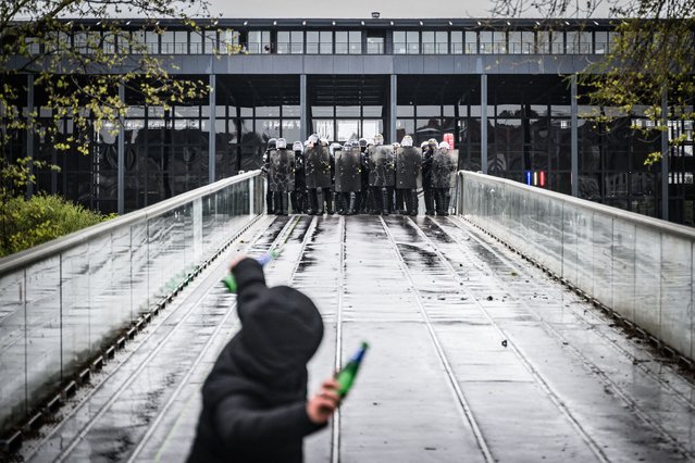 A protester throws a bottle towards riot police and French CRS riot police during a demonstration on the 12th day of action after the government pushed a pensions reform through parliament without a vote, using the article 49.3 of the constitution, in Nantes, western France on April 13, 2023. France faced nationwide protests and strikes on April 13, 2023, to denounce the French government's pension reform on the eve of a ruling from France's Constitutional Council on the reform. (Photo by Loic Venance/AFP Photo)