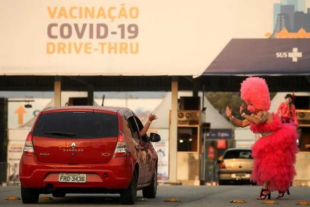 A drag queen waves to a car at a vaccine drive-thru as Sao Paulo begins to vaccinate young people from 18 to 21 years old against the coronavirus disease (COVID-19), in Sao Paulo, Brazil on August 14, 2021. (Photo by Carla Carniel/Reuters)