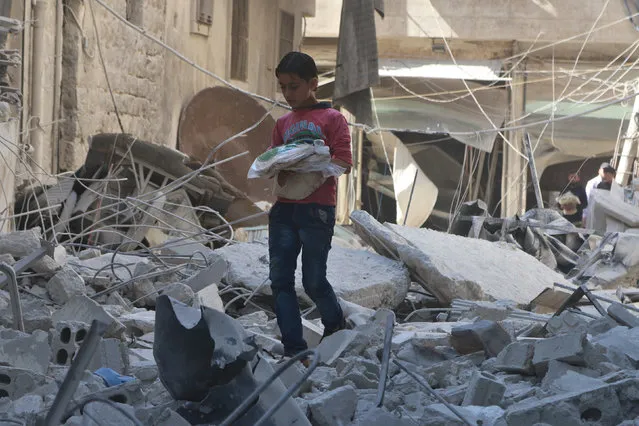 A boy carries bread as he makes his way through rubble of a site hit by an airstrike in the rebel held area of Aleppo's al-Sukari district, Syria, May 30, 2016. (Photo by Abdalrhman Ismail/Reuters)