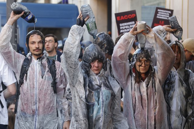 Climate protesters pour oil over them as scuffles between police and protesters broke out with the use of tear gas during a demonstration on the outskirts of the Paris venue for TotalEnergies Annual General Meeting in Paris on May 26, 2023. The French oil and gas giant is gearing up for an electric meeting, targeted by a coalition of associations threatening to block it, but also by some of its shareholders who disagree with its climate policy. (Photo by Geoffroy Van der Hasselt/AFP Photo)