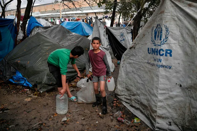 Boys carry water in the makeshift migrant camp after a rainfall hit the island of Chios on December 11, 2019 where thousands of refugees and migrants live in squalid condition, without water and electricity while winter has started. Officials on the three Greek islands hosting the country's largest migrant camps staged a walkout Wednesday to reject plans for larger facilities in an ongoing dispute with the government. According to government figures, there are over 40,000 asylum-seekers on the islands,in addition to over 20,000 people in camps on the mainland, which are nearly full or already past capacity. Hundreds more arrive daily. (Photo by Louisa Gouliamaki/AFP Photo)