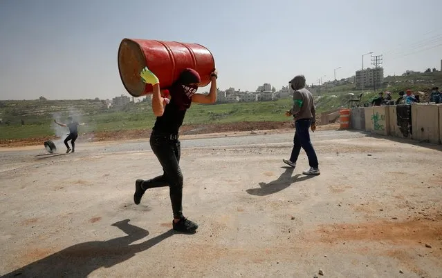 A Palestinian protester carries a barrel during clashes with Israeli forces near the Jewish settlement of Beit El, near Ramallah, in the Israeli-occupied West Bank, April 11, 2022. (Photo by Mohamad Torokman/Reuters)