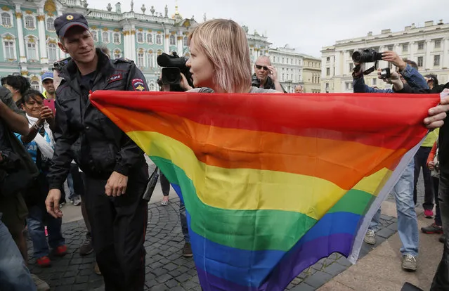 A gay rights activist stands with a rainbow flag, in front of journalists, during a protesting picket at Dvortsovaya (Palace) Square in St.Petersburg, Russia, Sunday, August 2, 2015. Several gay rights activists stood protesting against gay rights violation at Palace square where paratroopers celebrated Paratroopers' Day. (Photo by Dmitry Lovetsky/AP Photo)
