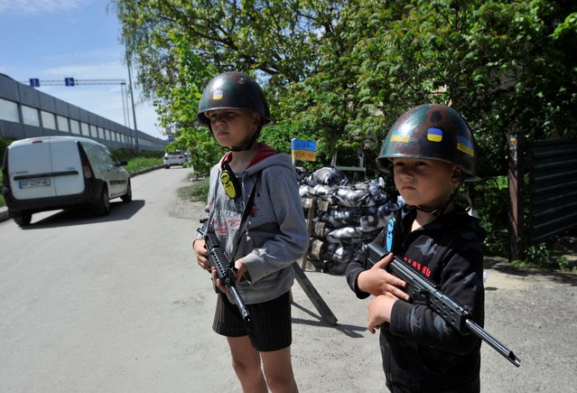 Ukrainian children play territorial defence fighters at a fake “checkpoint” in the willage of Stoyanka, Kyiv region on May 19, 2022, amid Russian invasion of Ukraine. (Photo by Sergei Chuzavkov/AFP Photo)