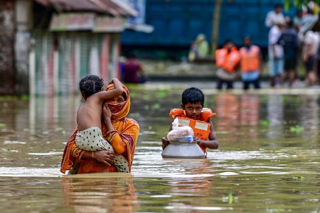 People wade through flood waters after collecting relief materials in Feni, in south-eastern Bangladesh, on August 24, 2024. Nearly 300,000 Bangladeshis were taking refuge in emergency shelters on August 24 from floods that inundated vast areas of the low-lying South Asian country, disaster officials said. The floods were triggered by heavy monsoon rains and have killed at least 42 people in Bangladesh and India since the start of the week, many in landslides. (Photo by Munir Uz Zaman/AFP Photo)