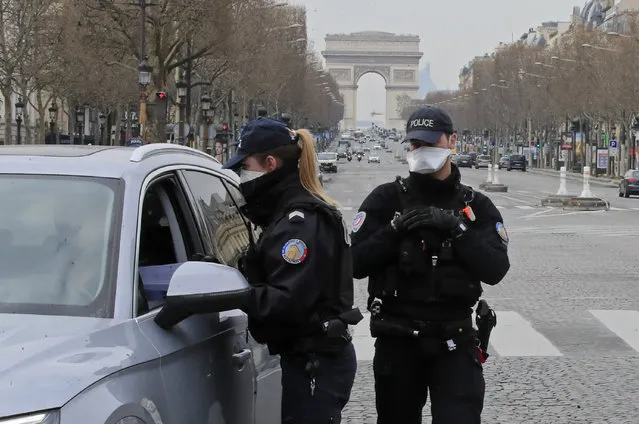 Police officers wearing protective masks check papers at a control point at the Champs Elysees avenue in Paris, Tuesday, March 17, 2020. France is imposing nationwide restrictions on how far from their homes people can go and for what purpose as part of the country's strategy to stop the spread of the new coronavirus. (Photo by Michel Euler/AP Photo)