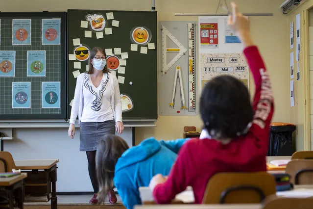 A teacher wearing protective face mask as she teaches close to pupils at a primary school in Morges, Switzerland, Monday, May 11, 2020. Swiss primary and secondary schools reopened with half of the students during the ongoing coronavirus Covid-19 pandemic. (Photo by Laurent Gillieron/Keystone via AP Photo)