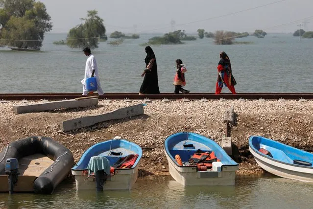 A displaced family walk along a railway track, past boats amid flood water, following rains and floods during the monsoon season in Sehto village on the outskirts of Sehwan, Pakistan on September 15, 2022. (Photo by Akhtar Soomro/Reuters)