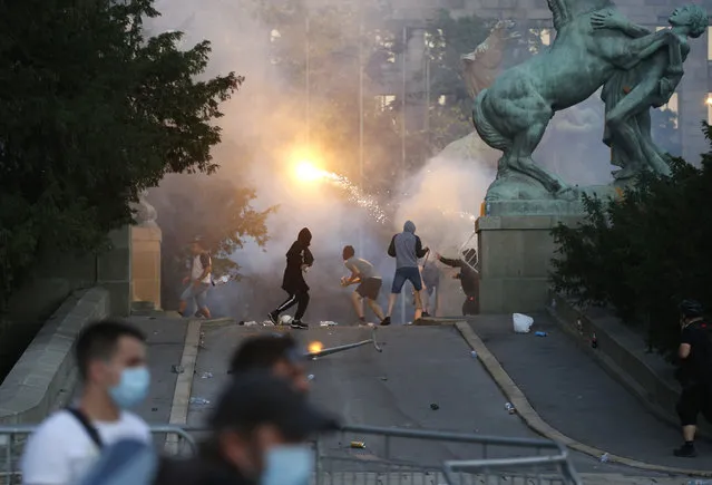 Protesters clash with Serbian riot police in Belgrade, Serbia, Wednesday, July 8, 2020. Police have fired tear gas at protesters in Serbia's capital during the second day of demonstrations against the president's handling of the country's coronavirus outbreak. President Aleksandar Vucic backtracked on his plans to reinstate a coronavirus lockdown in Belgrade this week, but it didn't stop people from firing flares and throwing stones while trying to storm the downtown parliament building. (Photo by Darko Vojinovic/AP Photo)