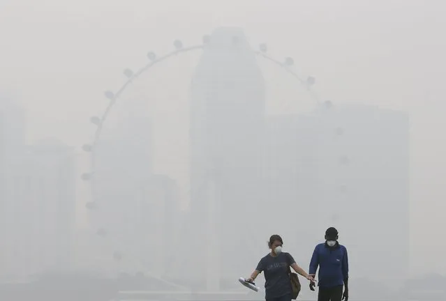 People wearing masks pass the Singapore Flyer Observatory Wheel shrouded by haze in Singapore September 29, 2015. (Photo by Edgar Su/Reuters)