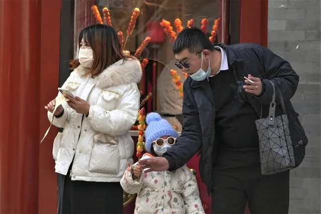 A couple buy a sugar-coated Chinese haw to a child at the Qianmen pedestrian shopping street, a popular tourist spot in Beijing, Tuesday, January 3, 2023. (Photo by Andy Wong/AP Photo)