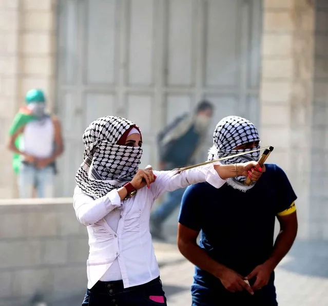 A Palestinian woman uses a slingshot during clashes with Israeli troops in the West Bank city of Bethlehem on Tuesday, October 13, 2015. A pair of Palestinian men boarded a bus in Jerusalem and began shooting and stabbing passengers, while another assailant rammed a car into a bus station before stabbing bystanders, in near-simultaneous attacks Tuesday that escalated a monthlong wave of violence. (Photo by Pacific Press/SIPA Press)