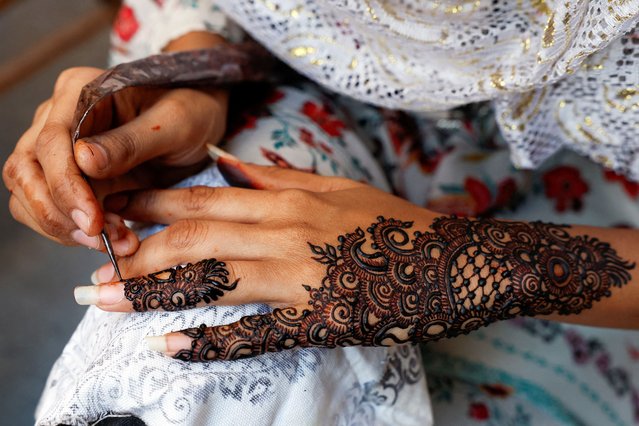 A girl applies henna patterns on her hands while waiting for customers, ahead of Eid al-Fitr celebrations, in Karachi, Pakistan on April 9, 2024. (Photo by Akhtar Soomro/Reuters)