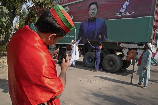 A supporter of former Prime Minister Imran Khan takes photos with mobile phone to his colleagues with huge Khan's poster painted on a truck neat the Khan's residence, in Lahore, Pakistan, Thursday, March 16, 2023. A Pakistani court on Thursday extended a pause for a day in an operation aimed at arresting the former premier Khan, a sign of easing tension in the country's cultural capital of Lahore where 24-hours-long clashes erupted this week when police tried to arrest Khan for failing to appear before a court in the capital. (Photo by K.M. Chaudary/AP Photo)