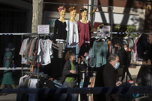 People walk by a clothes stall in the Rastro flea market in Madrid, Spain, Sunday, November 22, 2020. Madrid's ancient and emblematic Rastro flea market reopened Sunday after a contentious eight-month closure because of the COVID-19 pandemic that has walloped the Spanish capital. (Photo by Paul White/AP Photo)