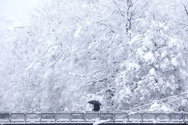 A man carrying an umbrella, crosses a bridge during heavy snowfall in Sarajevo, Bosnia, Monday, February 27, 2023. (Photo by Armin Durgut/AP Photo)