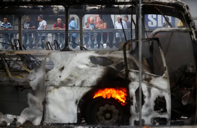 People look at a burned bus near a protest against the Rio de Janeiro state government and a plan that will limit public spending in Rio de Janeiro, Brazil, November 16, 2016. (Photo by Ricardo Moraes/Reuters)
