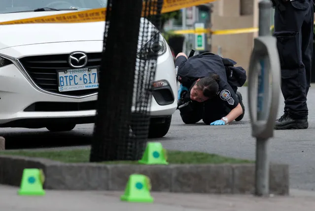 A police officer looks for evidence under a car while investigating a mass shooting on Danforth Avenue in Toronto, Canada on July 23, 2018. (Photo by Chris Helgren/Reuters)