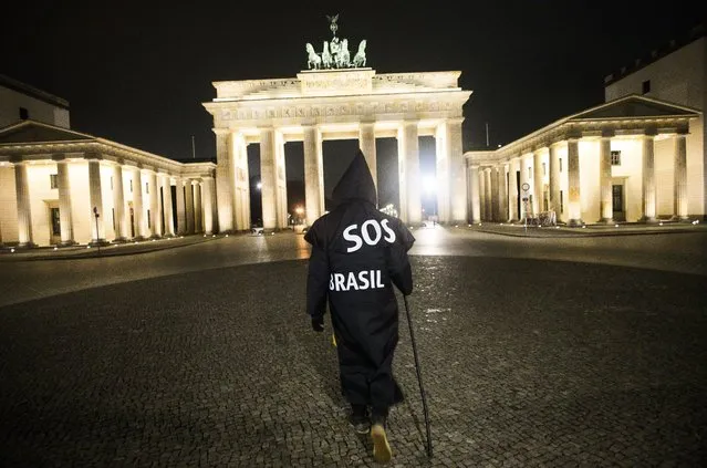 Brazilian activist and artist Rafael Puetter, dressed as the grim reaper, walks in front of the Brandenburg Gate in a one-man protest through Berlin, Germany, early Wednesday, April 7, 2021. The multimedia artist starts his performance at the Brazilian embassy in Berlin at midnight every night to protest against Brazil's COVID-19 policies. Rafael Puetter walks to the Brandenburg Gate and then to the nearby German parliament building, in front of which he counts out a sunflower seed to represent each of the lives that were lost over the past 24 hours in Brazil because of the coronavirus pandemic. (Photo by Markus Schreiber/AP Photo)
