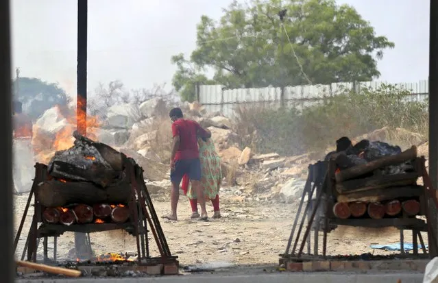 Family members of COVID-19 victims leave as their funeral pyres burn at an open crematorium set up at a granite quarry on the outskirts of Bengaluru, India, Wednesday, May 5, 2021. (Photo by Aijaz Rahi/AP Photo)