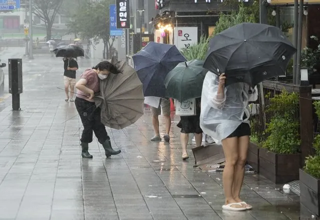 People struggle to hold onto their umbrellas in the rain and wind as the tropical storm named Khanun approaches to the Korean Peninsular, in Busan, Thursday, August 10, 2023. (Photo by Ahn Young-joon/AP Photo)