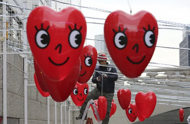 A worker decorates bulbs on a wire as balloons on display to celebrate upcoming Christmas season over the Cheonggye Stream in Seoul, South Korea, Monday, December 12, 2016. (Photo by Ahn Young-joon/AP Photo)
