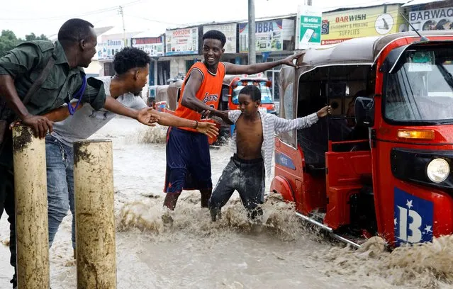 A child is assisted as he disembarks from a rickshaw taxi in the flooded KM5 street following heavy rains in Mogadishu, Somalia on November 8, 2023. (Photo by Feisal Omar/Reuters)