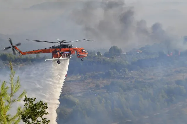 An helicopter drops water during a wildfire in ancient Olympia, western Greece, Thursday, Aug. 5, 2021. Greece evacuated people in boats from an island beach Wednesday amid heavy smoke from a nearby wildfire and fire crews fight elsewhere to keep flames away from the birthplace of the ancient Olympic Games as the country sweltered under a record heat wave. (Photo by Giannis Spyrounis/ilialive.gr via AP Photo)
