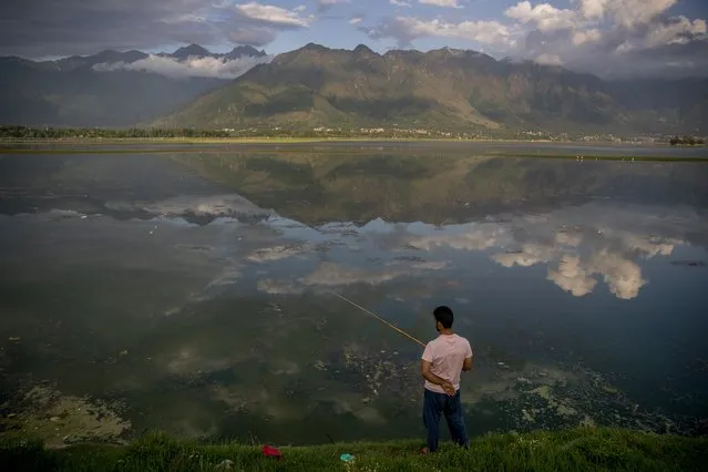 Clouds are reflected in water as a Kashmiri man fishes in the Dal Lake on the outskirts of Srinagar, Indian controlled Kashmir, Friday, July 30, 2021. (Photo by Dar Yasin/AP Photo)
