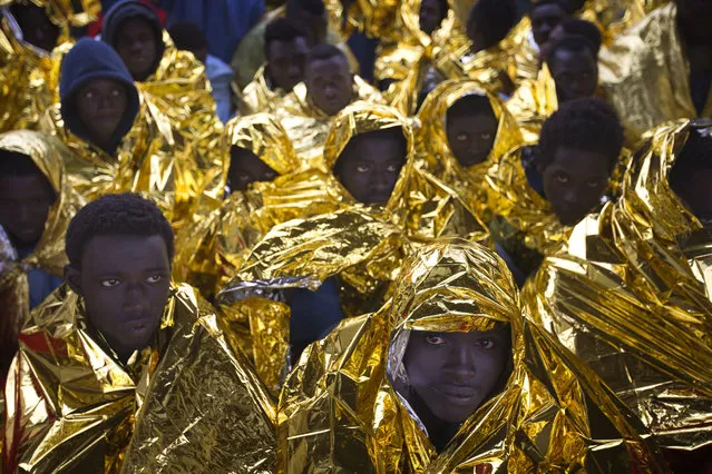 Wrapped in blankets, Sub-Saharan migrants sit on the deck of the Golfo Azzurro rescue vessel after arriving at the port of Messina, in Italy, with more than 299 migrants aboard the ship rescued by members of Proactive Open Arms NGO, on Sunday, January 29, 2017. (Photo by Emilio Morenatti/AP Photo)