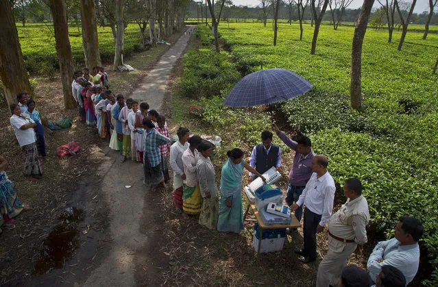 A woman casts her vote on the demo electronic voting machines and checks on Voter Verifiable Paper Audit Trail or VVPAT as others wait in the queue during an election awareness drive by district administration amongst the tea garden laborers ahead of India's general election in Jorhat, India, Monday, April 1, 2019. A VVPAT vending machine is an independent printing system connected to the electronic voting machines that allows voters to check that their votes are being cast as intended. The system will be used in the upcoming national elections to be held in seven phases starting from April 11. Votes will be counted on May 23. (Photo by Anupam Nath/AP Photo)