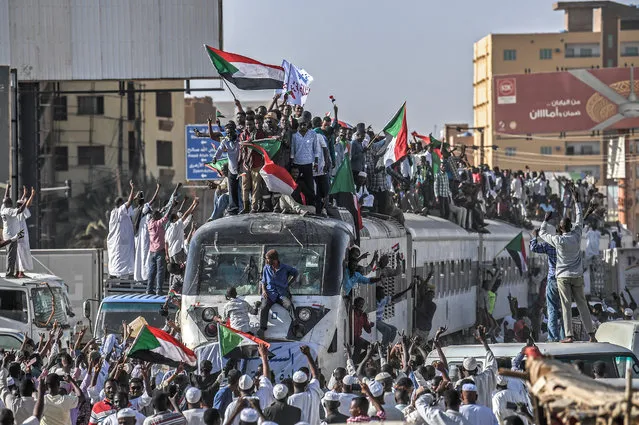 Sudanese protesters from the city of Atbara, sitting atop a train, cheer upon arriving at the Bahari station in Khartoum on April 23, 2019. The passengers, who had travelled from the town of Atbara where the first protest against ousted president Omar al-Bashir erupted on December 19, chanted "freedom, peace, justice". Many protesters perched on the roof of the train, waving Sudanese flags as it chugged through north Khartoum's Bahari railway station before winding its way to the protest site, an AFP photographer said. (Photo by Ozan Kose/AFP Photo)