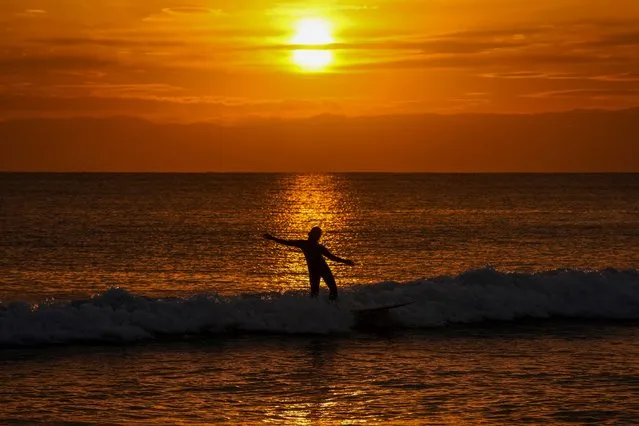 A surfer rides a waves as the sun sets Friday, December 10, 2021, in Fujisawa, South of Tokyo. (Photo by Kiichiro Sato/AP Photo)