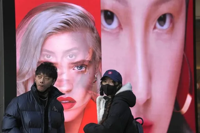 A woman wearing a mask stands near an ad featuring models for make up products in Beijing, China, Tuesday, December 28, 2021. Advertisements featuring some Chinese models have sparked feuding in China over whether their appearance and makeup are perpetuating harmful stereotypes of Asians. (Photo by Ng Han Guan/AP Photo)