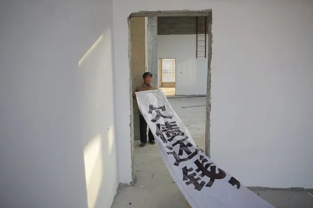 A migrant worker shows a banner inside a building that is under construction as a part of the Zixia Garden development complex in Qianan, Tangshan City, Hebei province, China January 28, 2016. The banner, which workers claim authorities told them not to use in their protests any more, reads “Pay back the money that you owe”. (Photo by Damir Sagolj/Reuters)