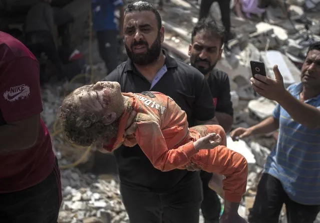 A Palestinian man carries a dead child taken out of the rubble of a destroyed residential building following Israeli airstrikes in Gaza City, Sunday, May 16, 2021. The Israeli airstrikes flattened three buildings and killed at least 26 people Sunday, medics said, making it the deadliest single attack since heavy fighting broke out between Israel and the territory's militant Hamas rulers nearly a week ago. (Photo by Khalil Hamra/AP Photo)