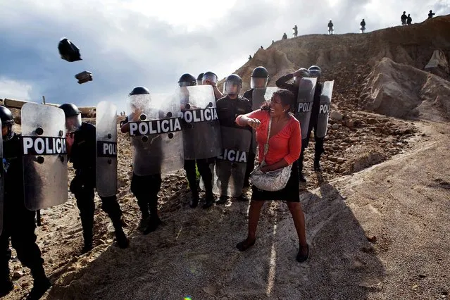 A woman throws a rock and a bag at policemen who block her way home in Peru's Madre de Dios region, on March 28, 2014. Soldiers, police and marines have begun enforcing a ban on illegal gold mining in Peru's southeastern jungle region, and miners clashed with police while intermittently blocking traffic on the Interoceanic Highway that links the Pacific with Brazil. (Photo by Rodrigo Abd/Associated Press)