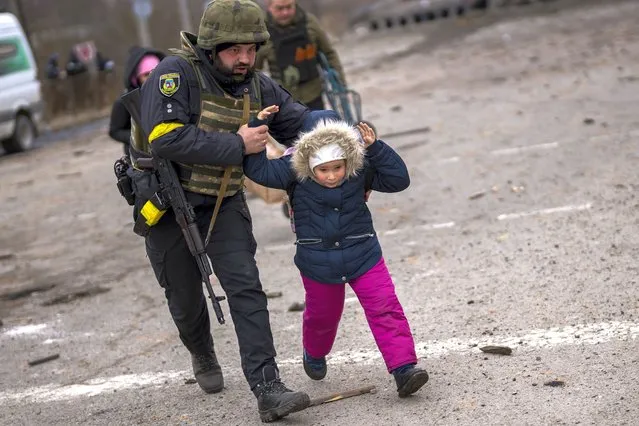 A Ukrainian police officer runs while holding a child as the artillery echoes nearby, while fleeing Irpin on the outskirts of Kyiv, Ukraine, Monday, March 7, 2022. (Photo by Emilio Morenatti/AP Photo)