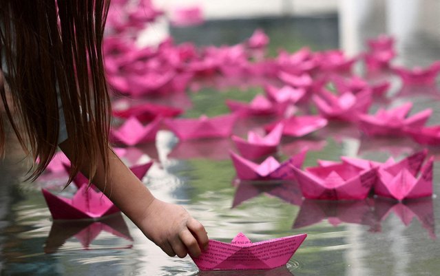 A child places a pink origami boat on water as part of “The Big One” event in London, Britain on April 23, 2023. (Photo by Henry Nicholls/Reuters)