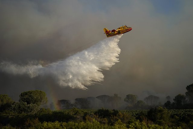 A water-dumping aircraft dumps water on a wildfire near Le Luc, southern France, Tuesday, August 17, 2021. Thousands of people fled homes, campgrounds and hotels near the French Riviera on Tuesday as firefighters battled a blaze that raced through nearby forests, sending smoke pouring down wooded slopes toward vineyards in the picturesque area. (Photo by Daniel Cole/AP Photo)